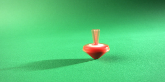 Ein sich drehender, roter Kreisel auf einem grünen Untergrund, mitten in der Bewegung eingefangen.