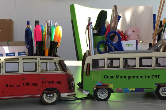 Schreibtischorga zwei Stifthalter in Form eines alten VB Bullis auf einem Schreibtisch. Darauf der Schriftzug "Service, Bildung, Forschung" und "Case Management ZBT"